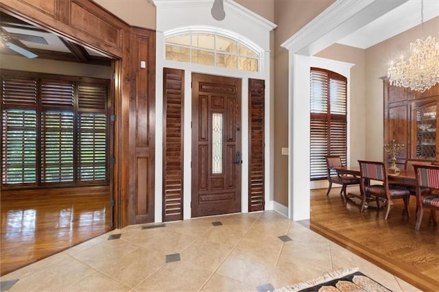 entryway featuring a healthy amount of sunlight, wood-type flooring, ceiling fan with notable chandelier, and ornamental molding