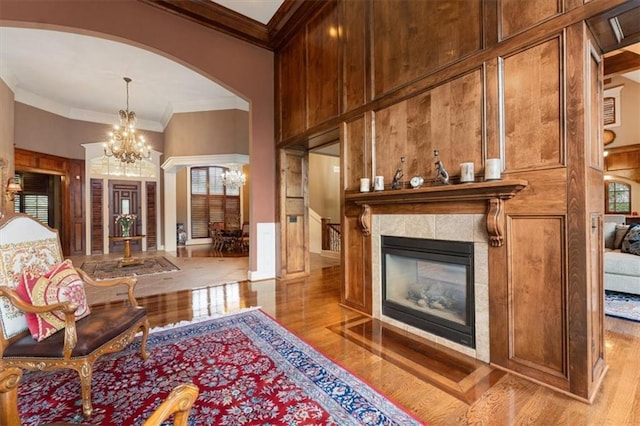 living area featuring a high ceiling, light wood-type flooring, a fireplace, ornamental molding, and a notable chandelier