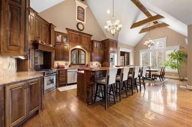 kitchen with appliances with stainless steel finishes, backsplash, high vaulted ceiling, a chandelier, and a kitchen island