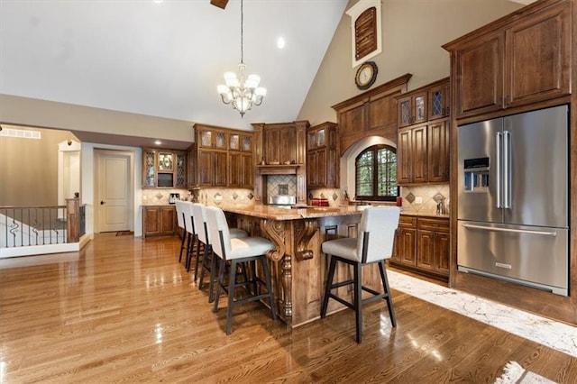 kitchen with light stone counters, high vaulted ceiling, a notable chandelier, high quality fridge, and a kitchen island