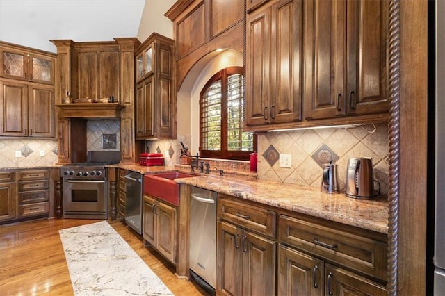 kitchen featuring vaulted ceiling, decorative backsplash, light wood-type flooring, light stone counters, and stainless steel appliances