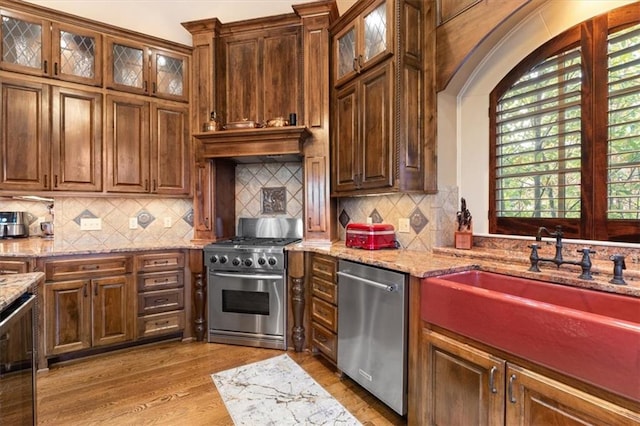 kitchen with decorative backsplash, light stone counters, light hardwood / wood-style flooring, and stainless steel appliances