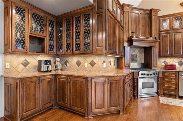 kitchen featuring appliances with stainless steel finishes, tasteful backsplash, light stone counters, custom range hood, and wood-type flooring