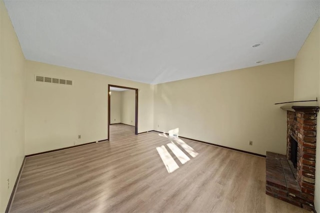 unfurnished living room featuring light wood-type flooring and a brick fireplace