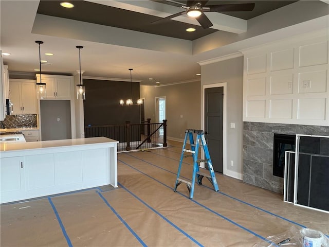 kitchen featuring a tray ceiling, tasteful backsplash, recessed lighting, a tiled fireplace, and white cabinetry