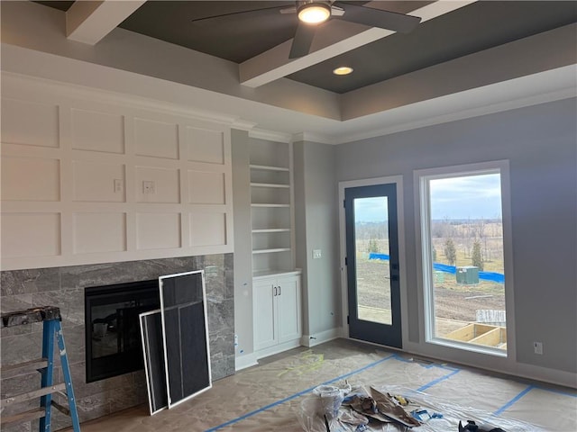 unfurnished living room with baseboards, a raised ceiling, crown molding, built in shelves, and a fireplace