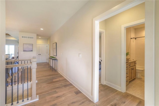 hallway with visible vents, baseboards, light wood-style flooring, an upstairs landing, and recessed lighting