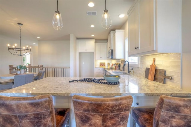 kitchen featuring light stone counters, a sink, visible vents, and white cabinets