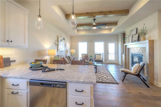 kitchen featuring stainless steel dishwasher, a glass covered fireplace, open floor plan, white cabinets, and hardwood / wood-style floors