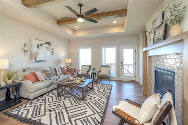 living room featuring a tray ceiling, beamed ceiling, a tiled fireplace, and wood finished floors