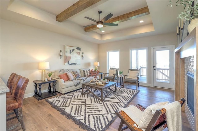 living room with a tray ceiling, beamed ceiling, baseboards, and wood finished floors