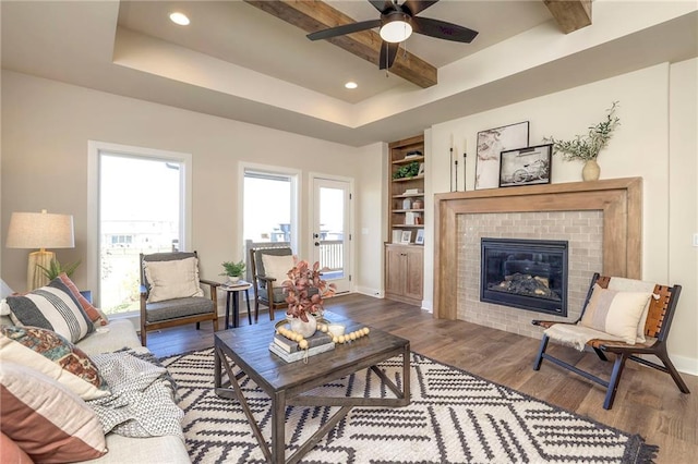 living area featuring built in features, beam ceiling, a fireplace, wood finished floors, and baseboards