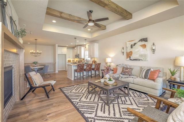 living room featuring recessed lighting, ceiling fan with notable chandelier, light wood-type flooring, a tray ceiling, and beamed ceiling