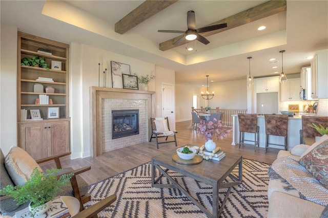 living area with recessed lighting, ceiling fan with notable chandelier, a fireplace, wood finished floors, and beam ceiling