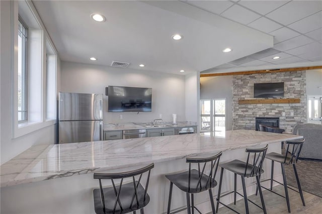 kitchen featuring visible vents, appliances with stainless steel finishes, light stone counters, a stone fireplace, and a sink