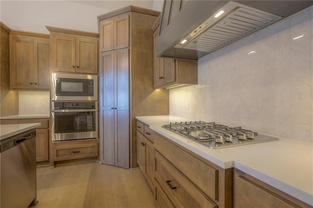 kitchen featuring premium range hood, appliances with stainless steel finishes, light hardwood / wood-style flooring, and backsplash