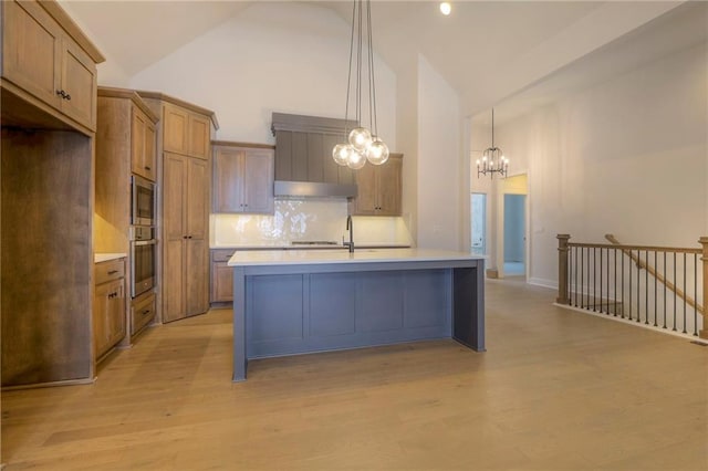 kitchen with pendant lighting, appliances with stainless steel finishes, a center island with sink, and light wood-type flooring