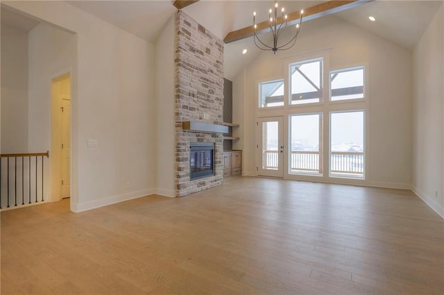 unfurnished living room with an inviting chandelier, a stone fireplace, high vaulted ceiling, and light wood-type flooring