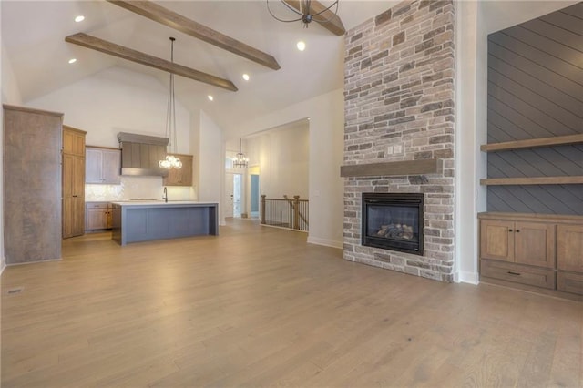 unfurnished living room with light hardwood / wood-style flooring, an inviting chandelier, high vaulted ceiling, a fireplace, and beamed ceiling