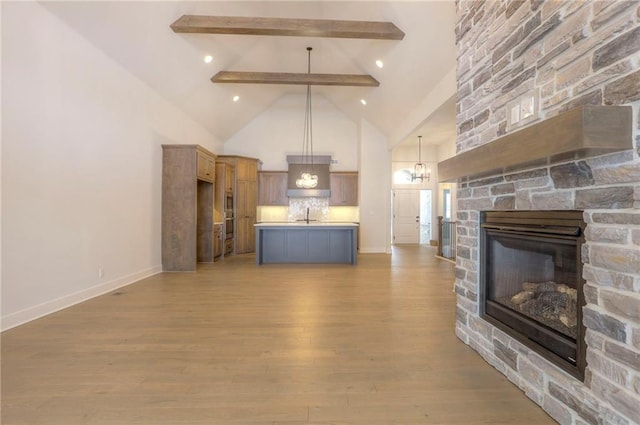 unfurnished living room with sink, light hardwood / wood-style flooring, high vaulted ceiling, a fireplace, and beamed ceiling