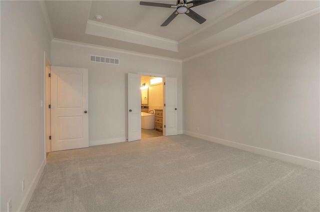 unfurnished bedroom featuring ornamental molding, light carpet, ensuite bath, and a tray ceiling