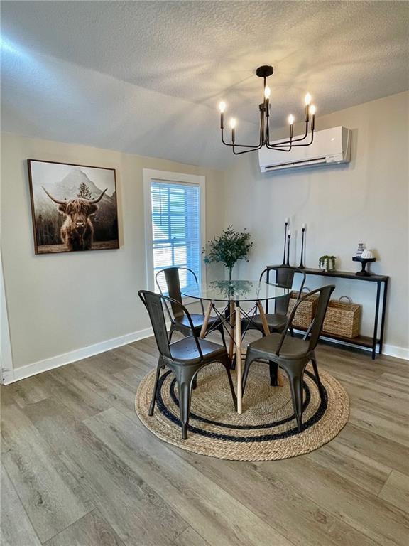 dining room with wood-type flooring, a wall unit AC, a notable chandelier, and a textured ceiling