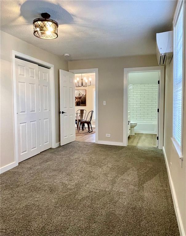 unfurnished bedroom with a closet, ensuite bathroom, a wall mounted AC, and carpet floors