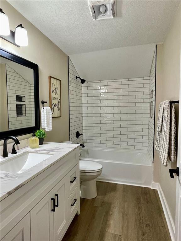 full bathroom with toilet, hardwood / wood-style floors, a textured ceiling, tiled shower / bath combo, and vanity