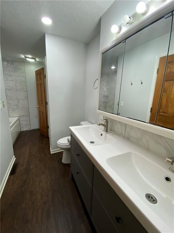 full bathroom featuring vanity, a textured ceiling, tiled shower / bath combo, hardwood / wood-style flooring, and toilet