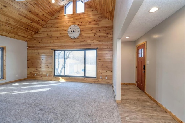 unfurnished living room featuring wood ceiling, wooden walls, high vaulted ceiling, and plenty of natural light