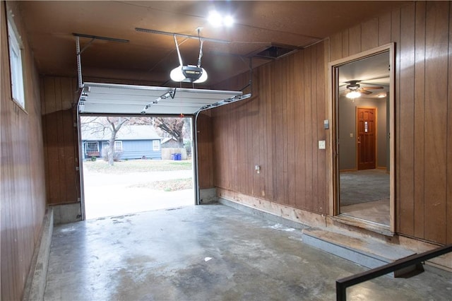 garage featuring wooden walls, ceiling fan, and a garage door opener