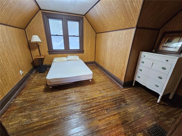 unfurnished bedroom featuring lofted ceiling, wooden walls, and dark wood-type flooring