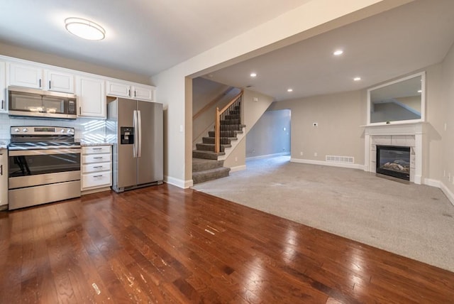 kitchen with decorative backsplash, appliances with stainless steel finishes, a tile fireplace, dark hardwood / wood-style floors, and white cabinetry