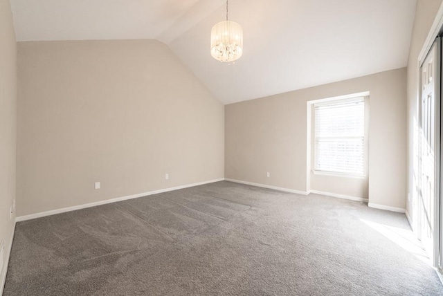 spare room with dark colored carpet, a notable chandelier, and lofted ceiling