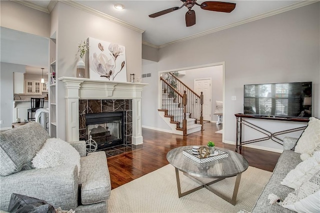 living room featuring a tiled fireplace, ceiling fan, dark hardwood / wood-style flooring, and crown molding