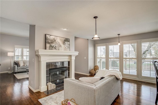 living room featuring a tiled fireplace, plenty of natural light, and dark hardwood / wood-style flooring