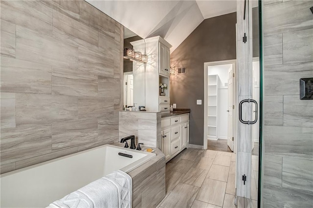 bathroom featuring vanity, tile walls, tiled bath, and vaulted ceiling