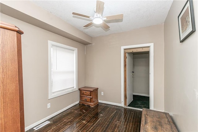 unfurnished bedroom with a textured ceiling, ceiling fan, a spacious closet, dark hardwood / wood-style floors, and a closet