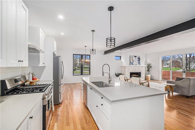 kitchen with stainless steel appliances, white cabinetry, a kitchen island with sink, and pendant lighting