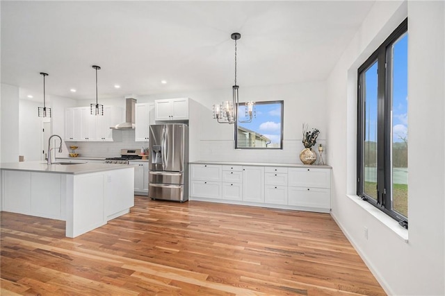 kitchen with pendant lighting, wall chimney range hood, sink, appliances with stainless steel finishes, and white cabinetry