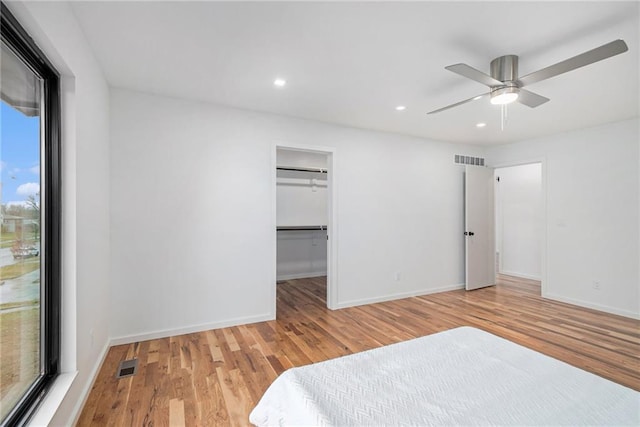 unfurnished bedroom featuring ceiling fan, a walk in closet, and light wood-type flooring