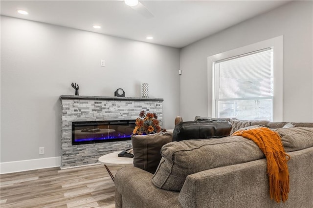 living room featuring ceiling fan, a stone fireplace, and wood-type flooring