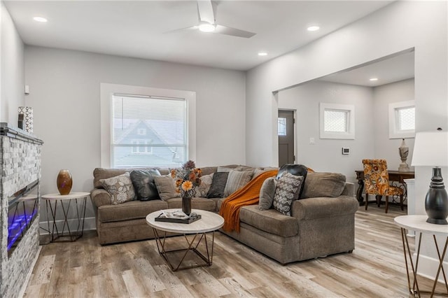 living room with ceiling fan, a stone fireplace, and light wood-type flooring