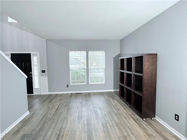 unfurnished living room with baseboards, wood finished floors, and stairway