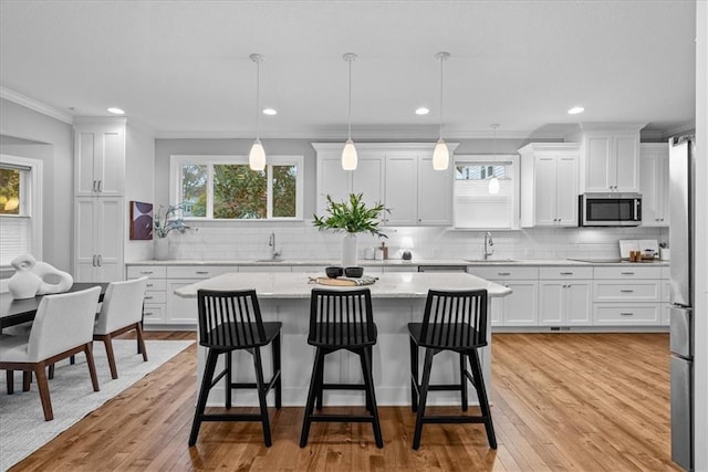 kitchen featuring white cabinets, decorative light fixtures, stainless steel appliances, and light hardwood / wood-style flooring