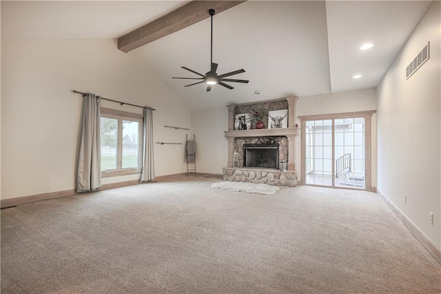 unfurnished living room featuring ceiling fan, beam ceiling, a stone fireplace, and a wealth of natural light