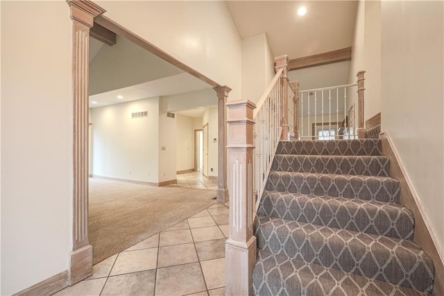 staircase featuring tile patterned floors, ornate columns, and high vaulted ceiling