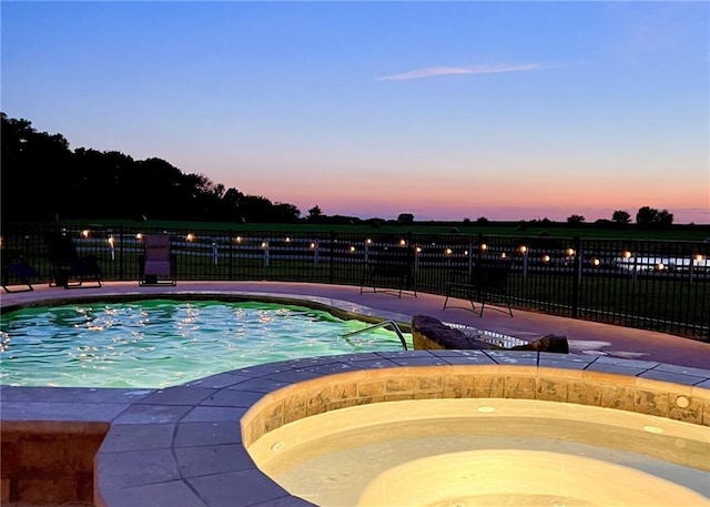 pool at dusk featuring an in ground hot tub