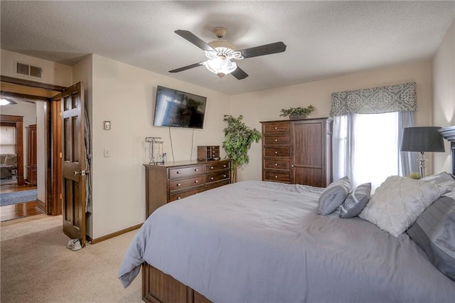 bedroom with ceiling fan, light colored carpet, and a textured ceiling