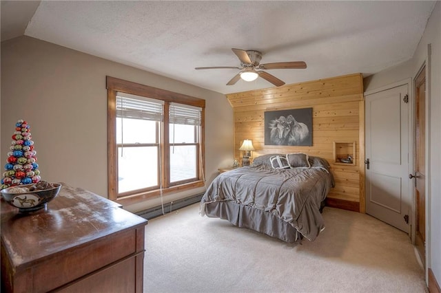 bedroom with wood walls, vaulted ceiling, ceiling fan, a baseboard radiator, and light colored carpet